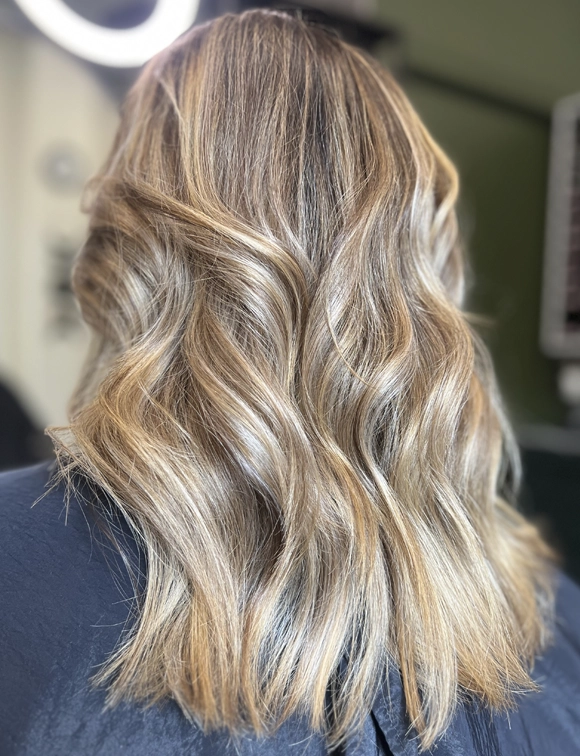 Close-up back view of a woman's blonde wavy hair with natural highlights and lowlights, showing depth and texture.