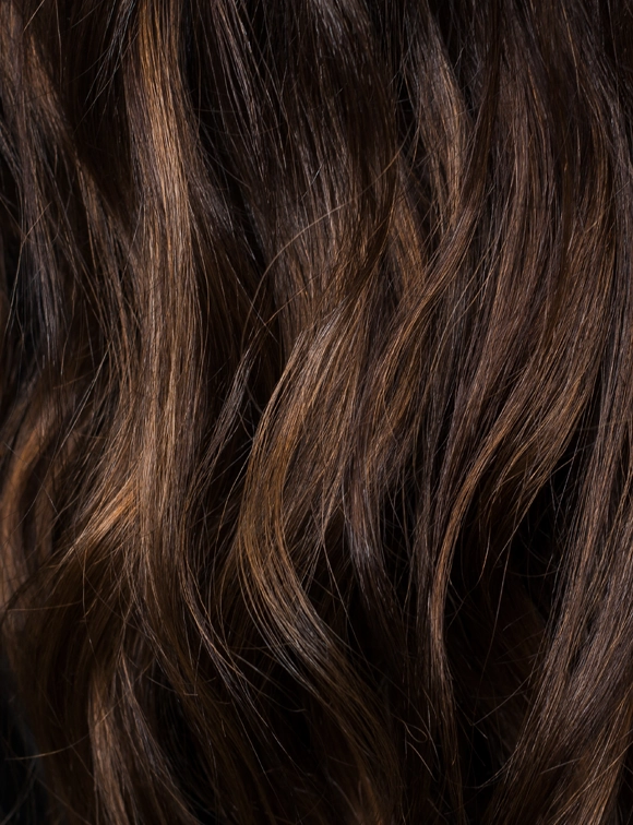 Close-up back view of a woman's dark brown wavy hair with natural highlights and lowlights, showing depth and texture.